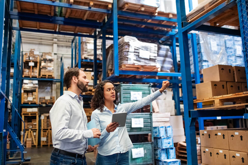 Businesswoman with a digital tablet showing and talking with male worker in distribution warehouse. Manager working with foreman in warehouse checking stock levels.