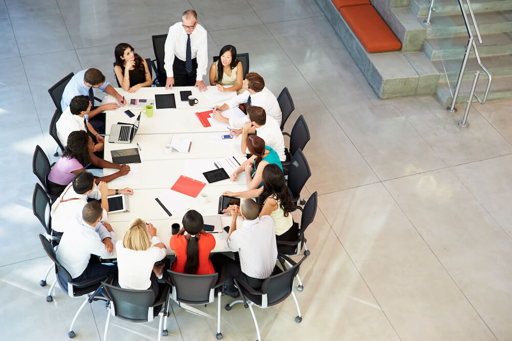Businessman Addressing Work Colleagues In Meeting Around Boardroom Table